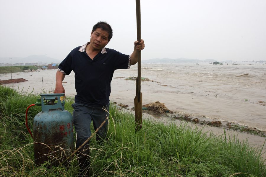 6月16日，一名男子手提液化气罐在浙江省诸暨市浦阳江水灾地区行走。